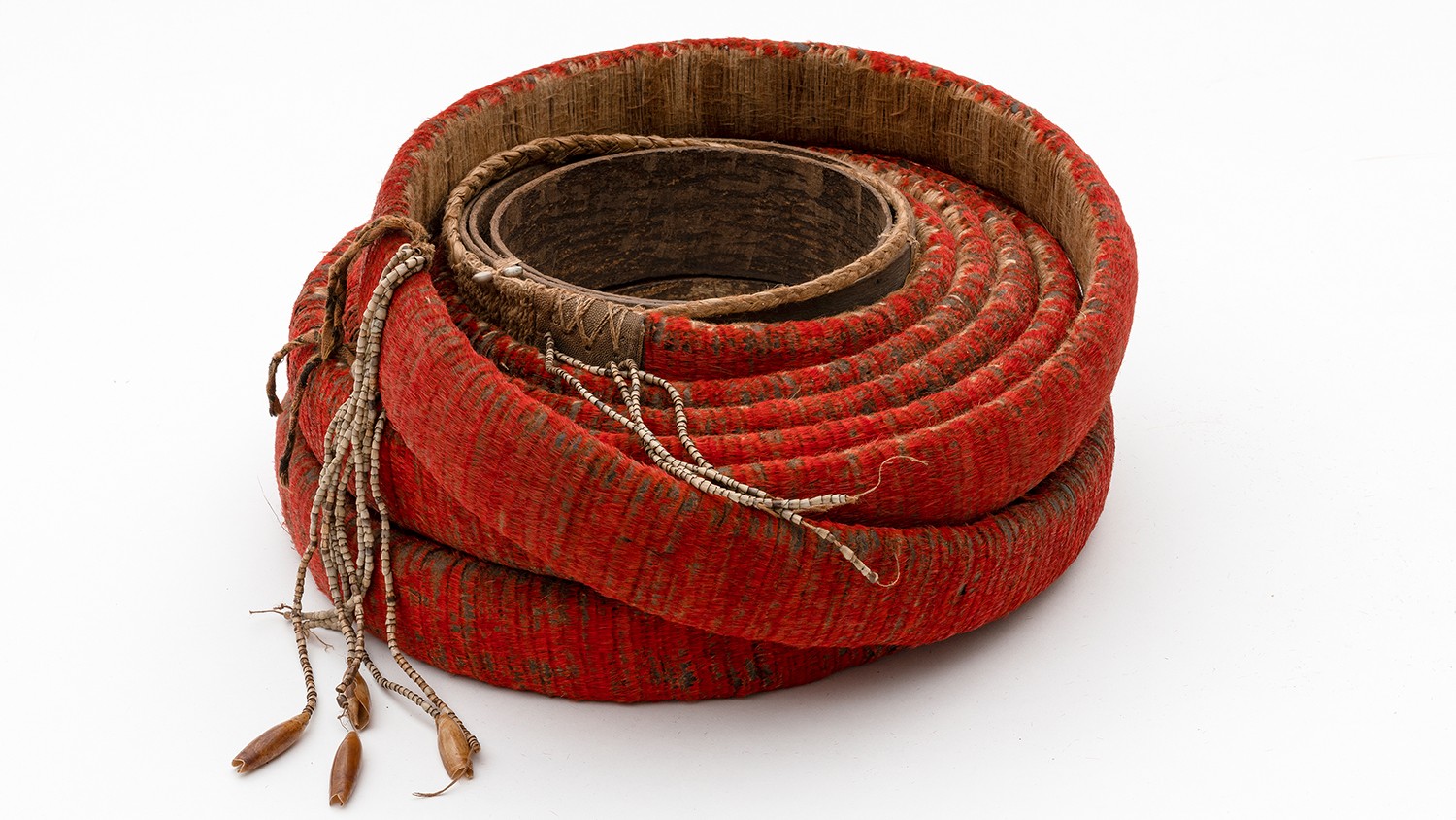 The intensive red of the feather money (mangahau) from the Melanesian Santa Cruz Islands is produced by the artful arrangement of up to 60,000 small cinnabar red feathers of the honeyeater (Myzomela Cardinalis). If the red fades over time, then the feather money roll also loses its value. Feathers, bark, barkcloth, snail shells, Job’s  tears seeds. Collected by Volker Schneider, 1980s.